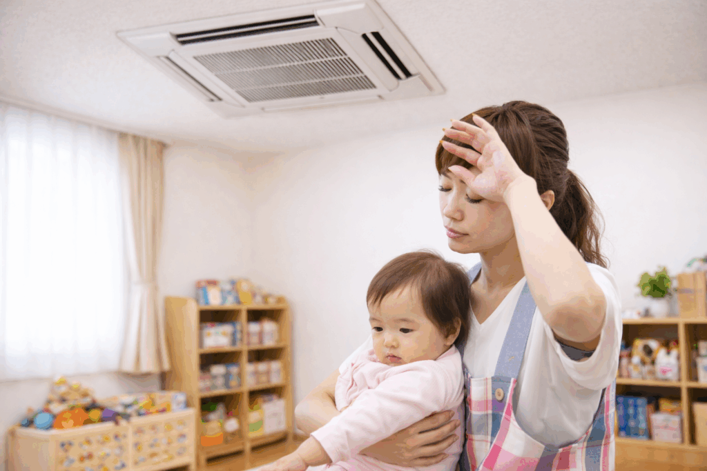 保育園の教室で暑そうにする保育士と赤ちゃん 天井カセット型エアコン