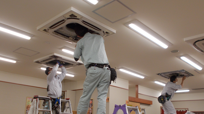 業務用エアコンの天井カセット型を分解し、内部の汚れを清掃している作業風景