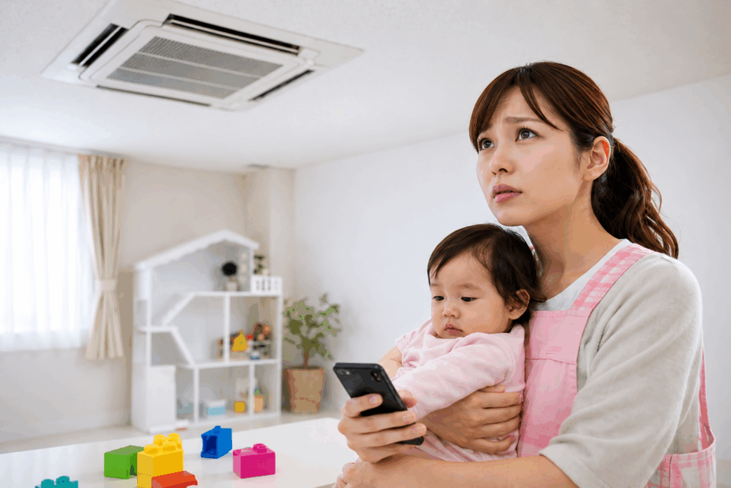 子どもを抱えた女性が天井の業務用エアコンを見上げながら室内環境を気にしている様子