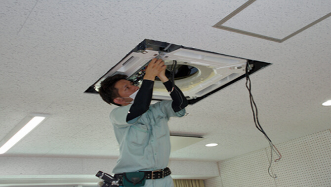 福岡市で天井カセット形業務用エアコンの内部部品を取り外す作業員