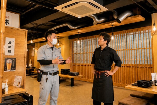 居酒屋の業務用エアコンを点検した専門業者から説明を受ける店長