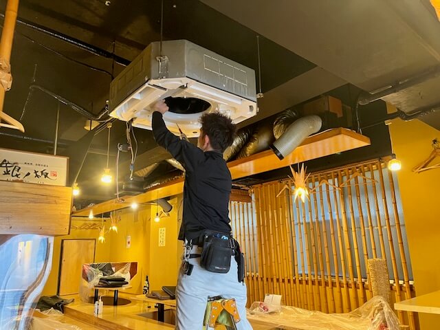 居酒屋で天井カセット型業務用エアコンを分解している作業員