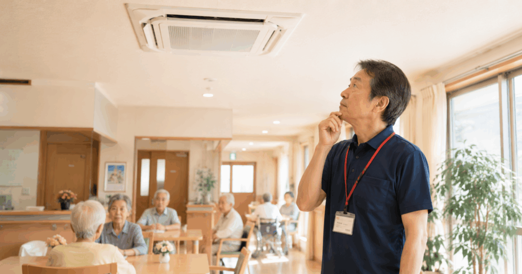 介護施設の食堂で業務用エアコンが停止し天井を確認する施設長
